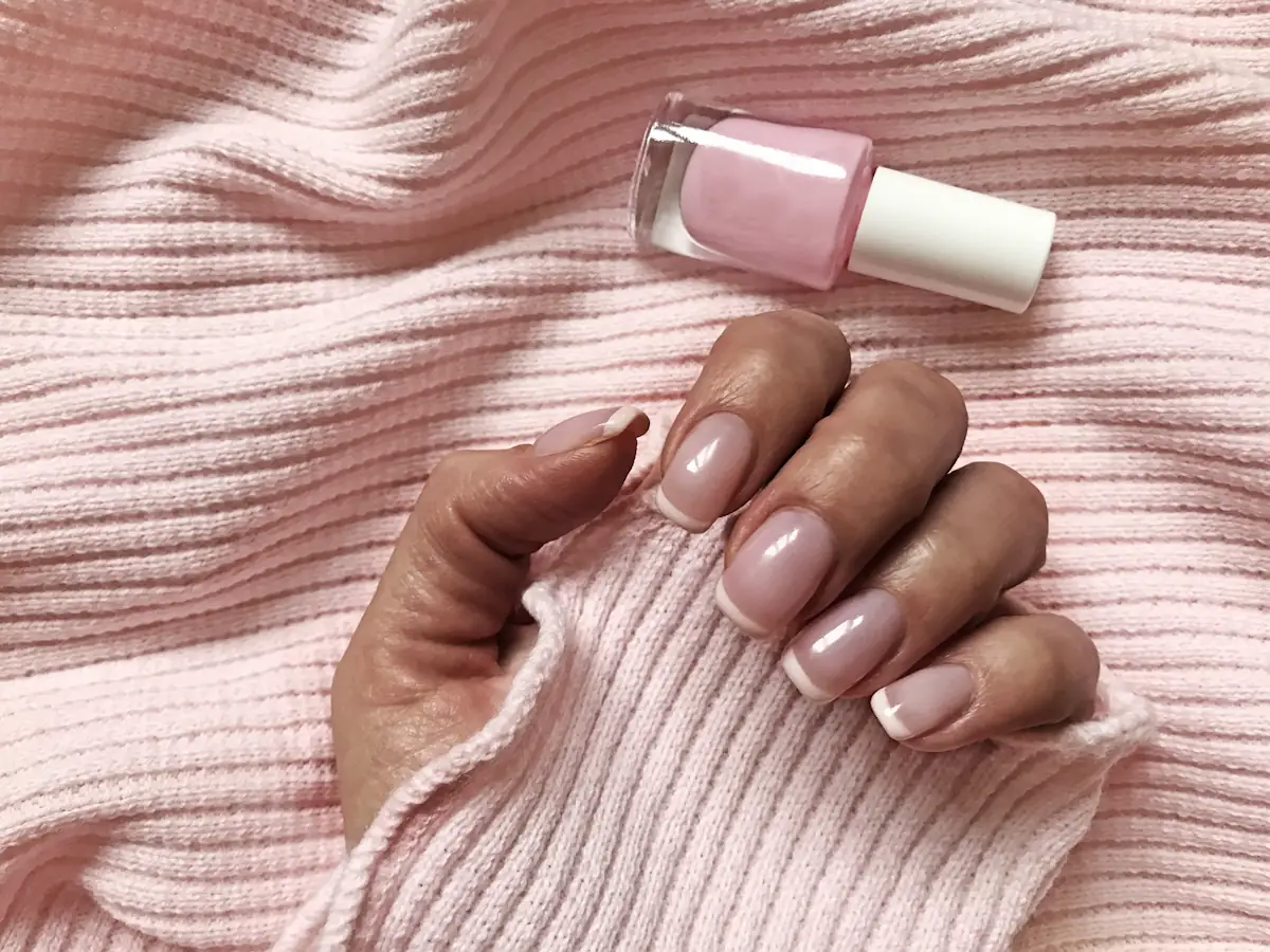 Une main avec des ongles colorés avec un vernis rose poudré très pâle